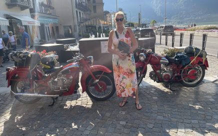 Femke in een zonnig Porlezza voor twee rode Moto Guzzi's.