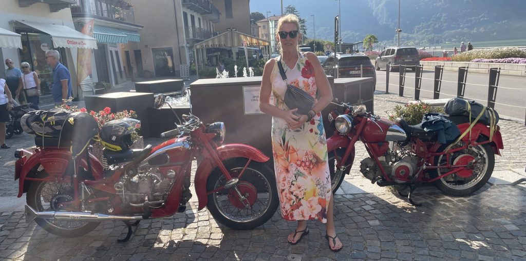 Femke in een zonnig Porlezza voor twee rode Moto Guzzi's.