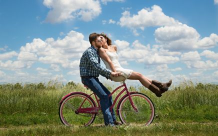 Foto van stel dat elkaar kust, zittend op een fiets. Hij zit op het zadel, zij op het stuur.