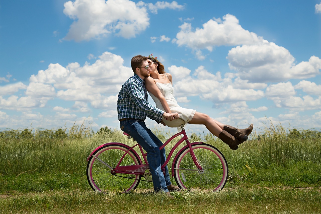 Foto van stel dat elkaar kust, zittend op een fiets. Hij zit op het zadel, zij op het stuur.